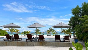 A beachside lounge with lounge chairs and umbrellas, palm trees, and a clear view of the ocean. - The Secret Garden Koh Rong (Koh Rong)