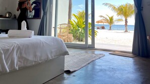 A hotel room with a bed, a large window with curtains, a view of the beach, and a chair outside. - The Secret Garden Koh Rong (Koh Rong)