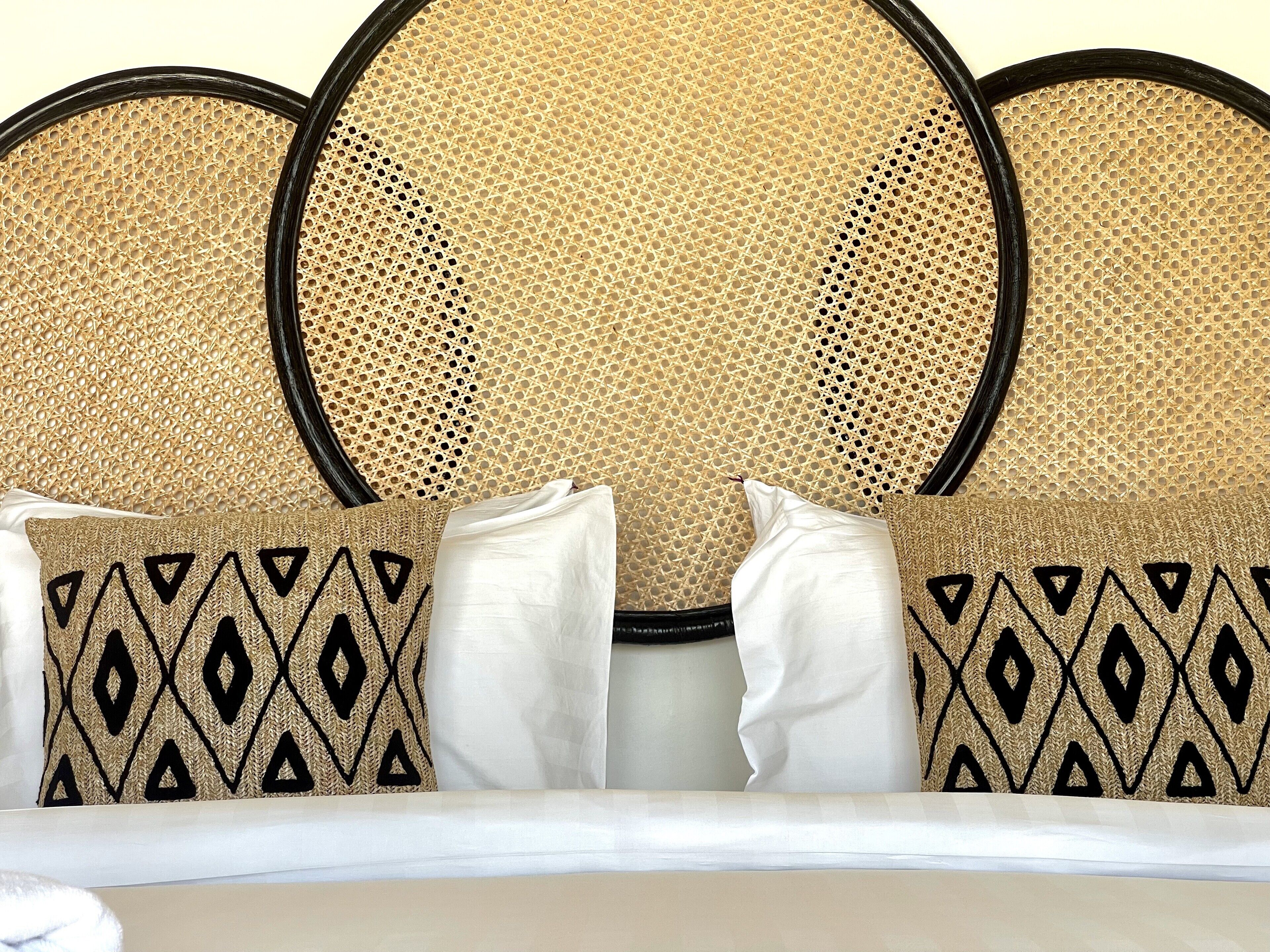 A bed with a rattan headboard and patterned pillows.