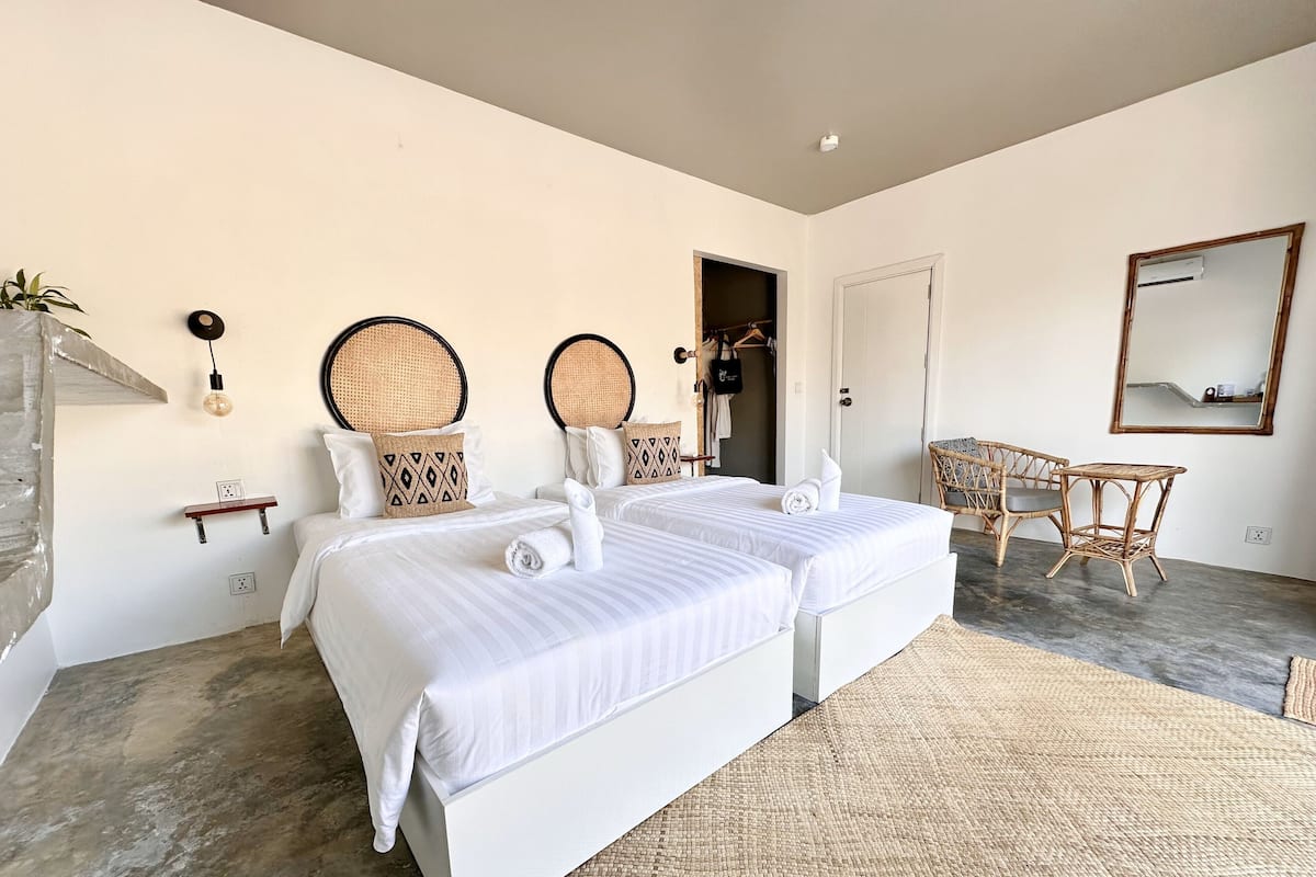 Habitación de hotel con dos camas, una mesita, una silla, un espejo y una lámpara fijada a la pared.