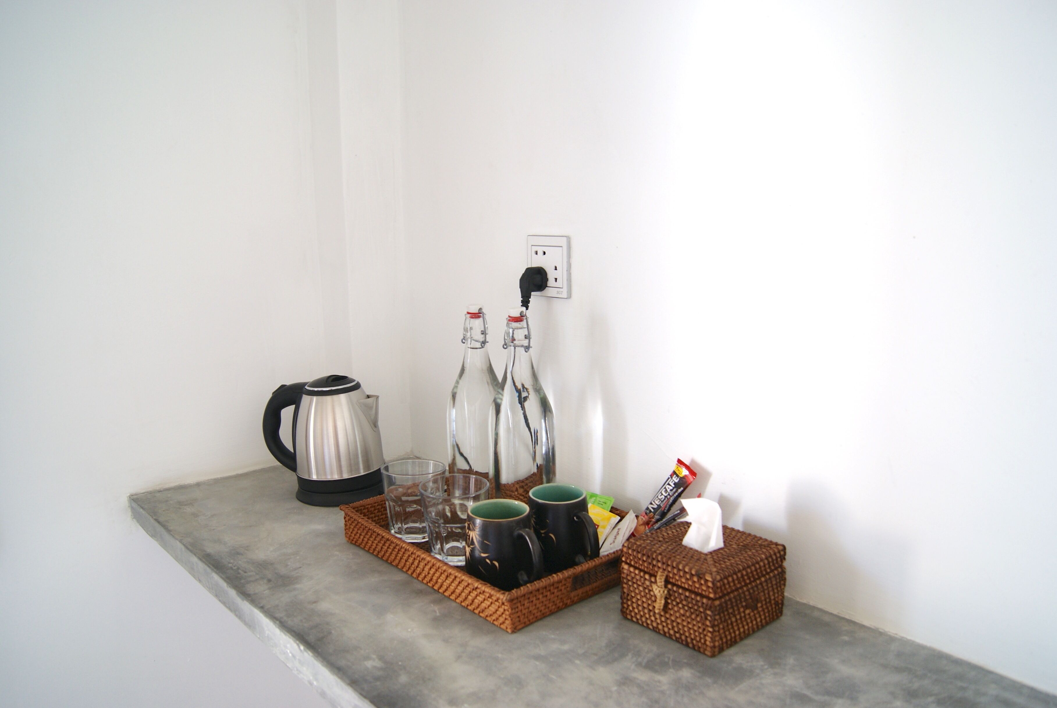 Una pequeña cocina americana con cafetera, dos tazas, hervidor y una cesta con pañuelos.