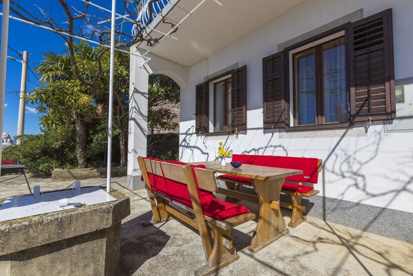 Un patio con mobiliario de madera y una pared blanca con ventanas.