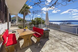 Un patio al aire libre con una mesa de madera y sillas rojas con cojines, con vista a un cuerpo de agua y una costa distante.