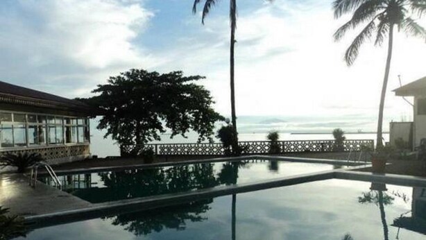 A swimming pool with a view of the ocean, surrounded by palm trees and a building with a balcony. - FINI Downtown (Limbe)