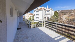 A balcony with stone flooring, a metal railing, and a view of residential buildings in the background. - Apartments Milan (Crikvenica)