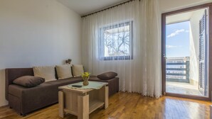 A living room with a brown sofa, a small wooden table with a vase, and a window with white curtains. - Apartments Milan (Crikvenica)