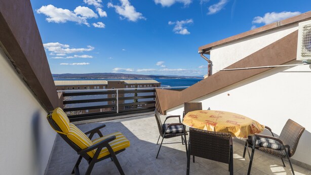 A balcony with a table and chairs, overlooking a coastal view. - Apartments Milan (Crikvenica)