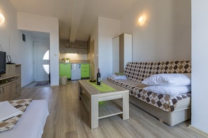 A compact living space with a sofa, a small table, a television, and a kitchen area in the background. - Apartments Milan (Crikvenica)
