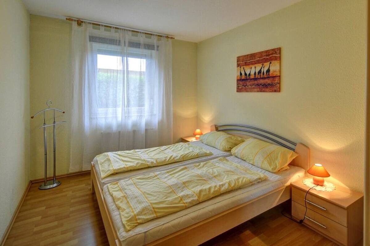 Un lit double avec deux tables de chevet, une fenêtre avec des rideaux légers et un tableau accroché au mur.
