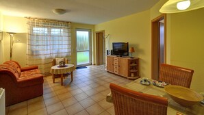 A living room with a sofa, a TV, a dining table with chairs, and a window with curtains. - Inselblume 41 - 42 (Fehmarn)