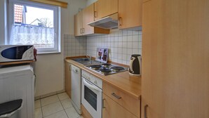 A compact kitchen with a microwave, stove, oven, sink, and wooden cabinets. - Inselblume 41 - 42 (Fehmarn)