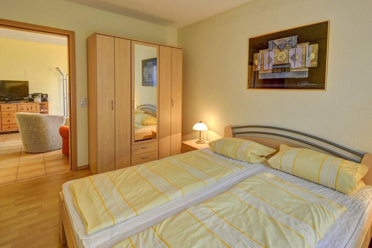 Une chambre à coucher comprenant un lit, une table de chevet, une lampe, une armoire et un tableau accroché au mur.