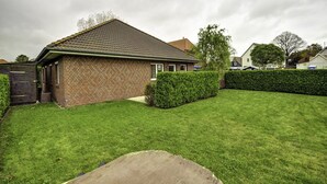 A single-story brick house with a tiled roof, a well-maintained lawn, and a wooden fence. - Inselblume 41 - 42 (Fehmarn)