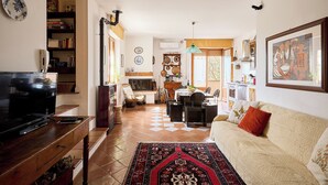 Een woonkamer met een televisie, bank en een eethoek met stoelen en een tafel.