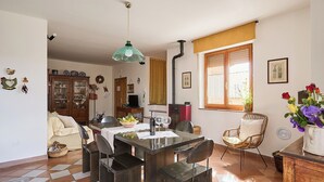 Een eetruimte met een tafel voor vier personen, omringd door stoelen, een hanglamp en een raam met gordijnen.