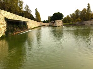 A stone bridge over a calm water body with a stone wall on one side and trees in the background. - Cosy flat with excellent location in Valencia! (Mislata)
