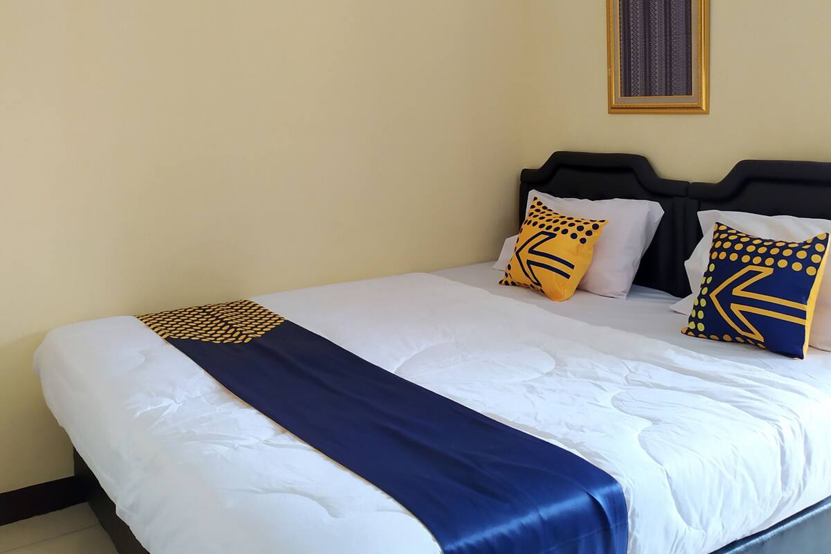 A hotel room with a bed, a headboard, and a wall-mounted air conditioner.