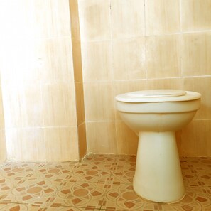A toilet in a bathroom with beige tiled walls and patterned floor tiles. - Hotel O Pondok Ripuji (Makassar)