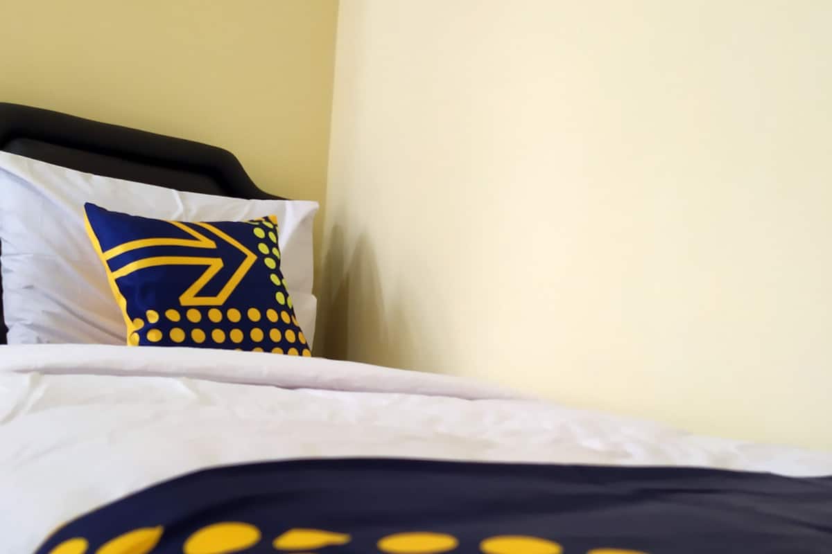 A bed with a white and navy blue bedspread featuring yellow polka dots, a navy blue pillow with a yellow arrow design, and a white pillow.