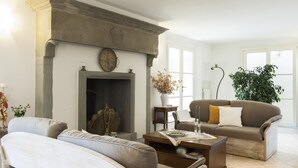 A living room with a fireplace, two sofas, a coffee table, and a large window. - Villa Caiano (Londa)