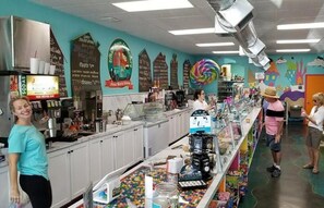 A brightly lit café with a counter, menu boards, and a colorful mural on the wall.