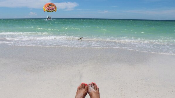 A beach with a parasail in the distance, a boat, and a bird on the shore.