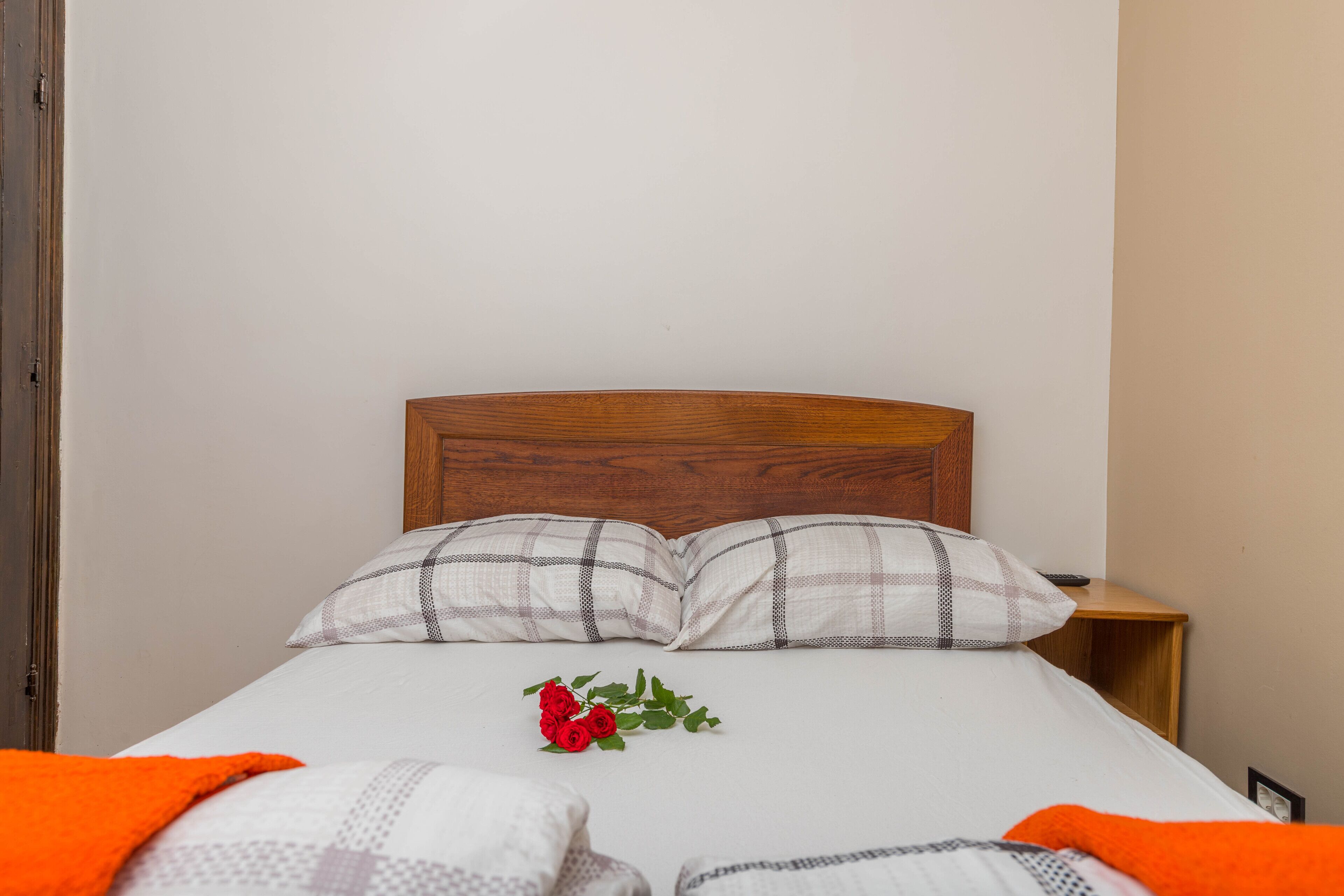 A neatly made bed with a wooden headboard, two pillows, and a single red rose on the bed.