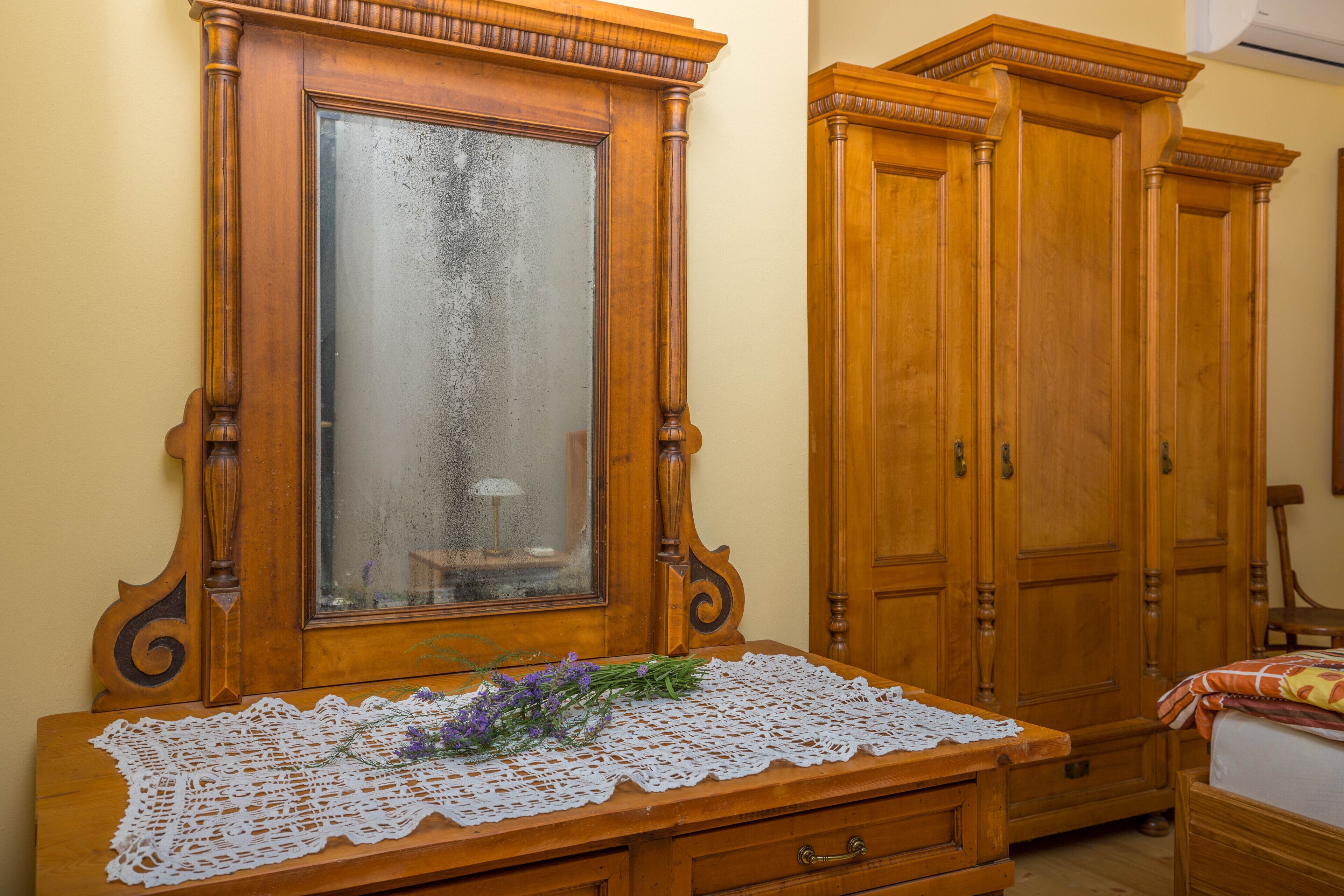 Un aparador de madera con espejo, un mantel de encaje y un ramo de flores.