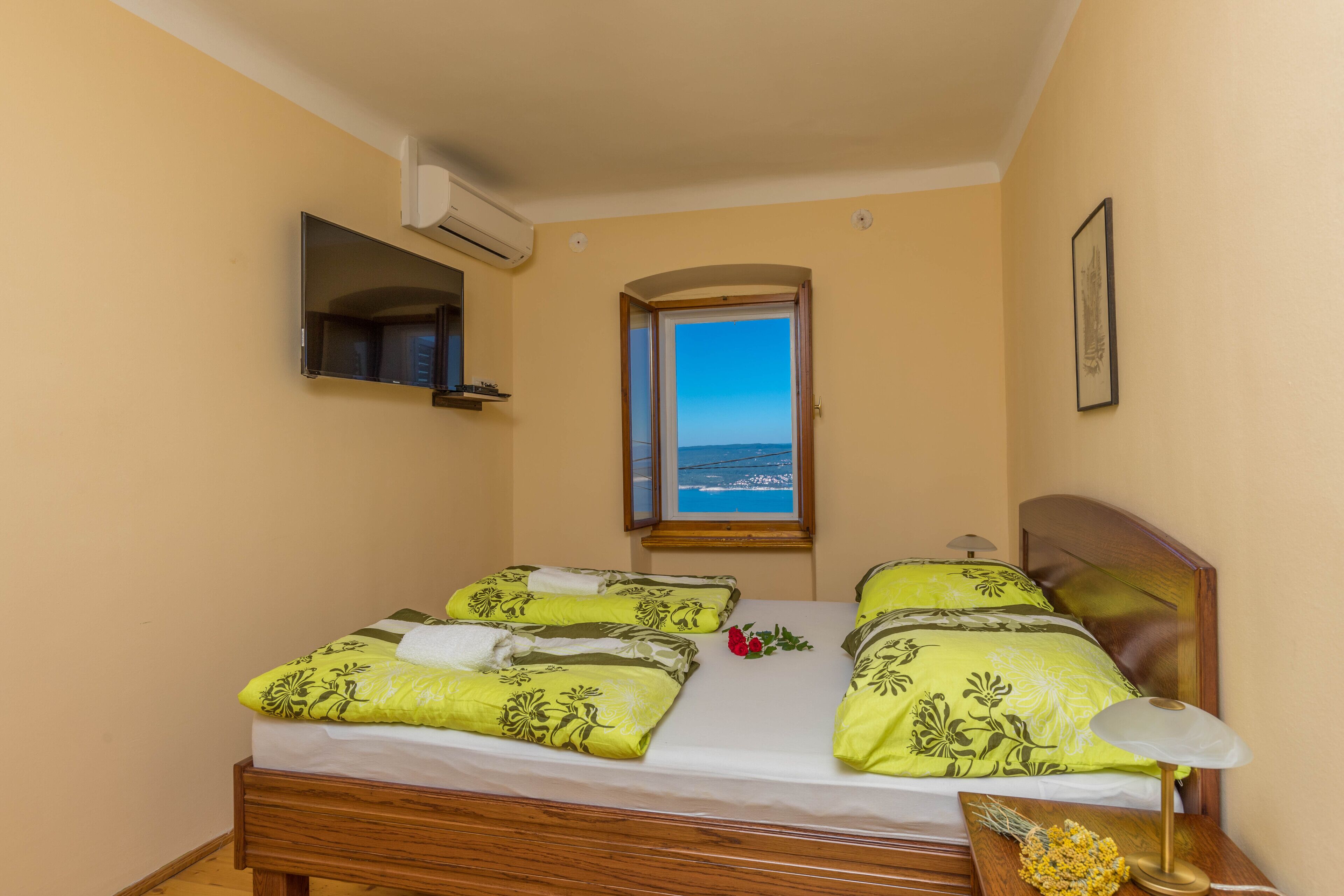 Una cama doble con ropa de cama floral, una mesita de noche con lámpara, una ventana con vistas y un equipo de aire acondicionado.