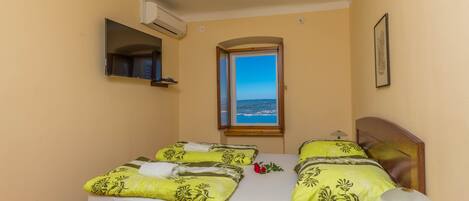 Una cama doble con ropa de cama floral, una mesita de noche con lámpara, una ventana con vistas y un equipo de aire acondicionado.