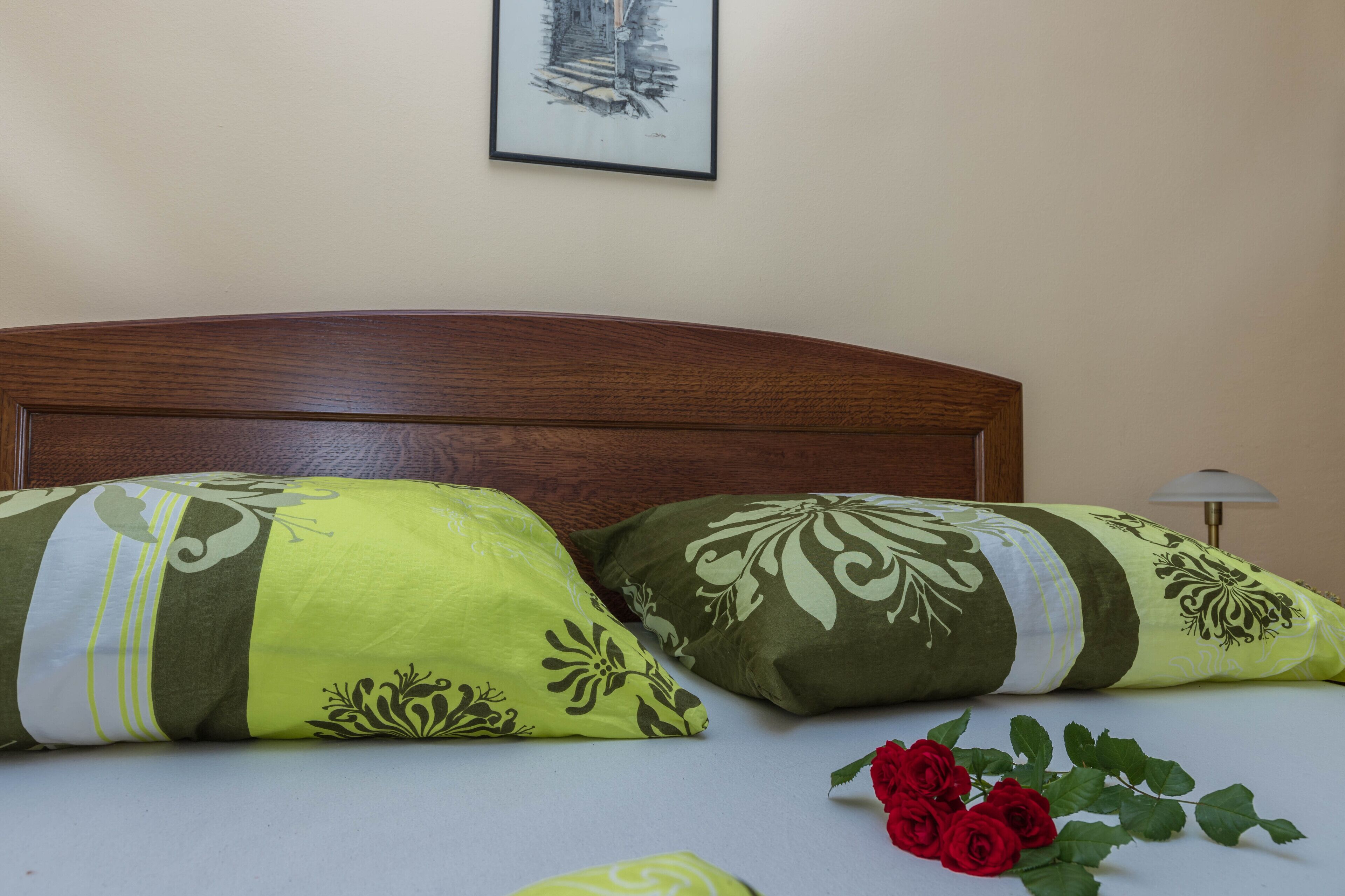 A bed with two decorative pillows, a framed picture on the wall, and a vase with red roses.