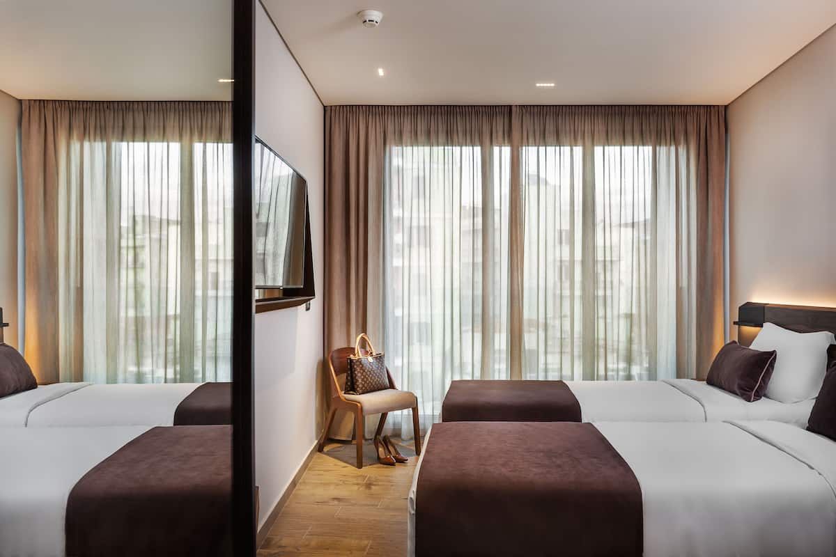Une chambre d’hôtel avec deux lits, une chaise, un téléviseur et de grandes fenêtres avec des rideaux.