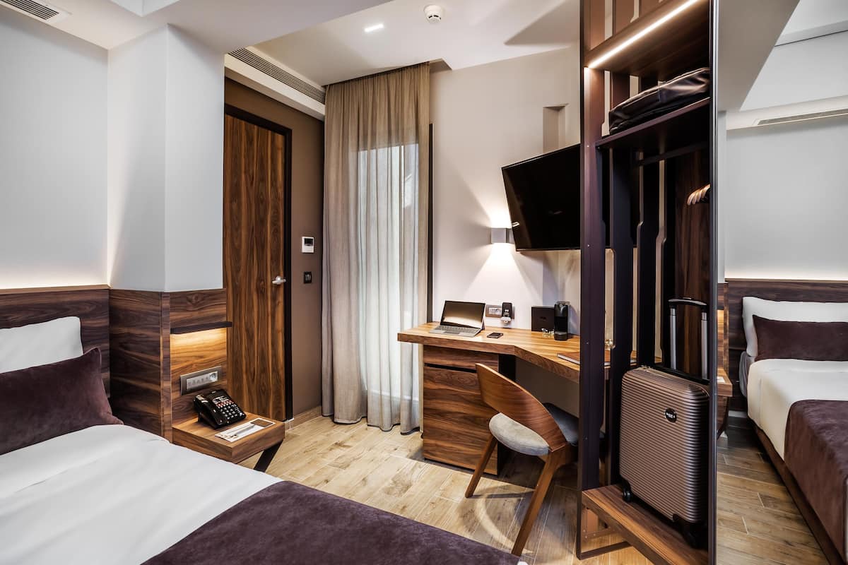 Une chambre d’hôtel équipée d’un lit, d’un bureau, d’une chaise, d’une télévision, d’une armoire et d’une valise.
