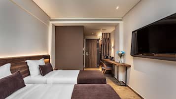 A modern hotel room with two beds, a desk, a TV, and a wooden floor.