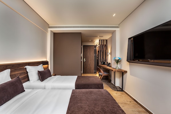 A modern hotel room with two beds, a desk, a TV, and a wooden floor.