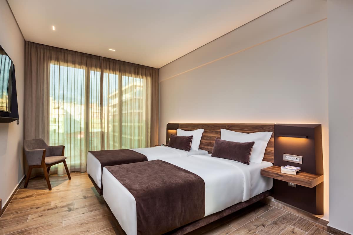 Une chambre d’hôtel moderne avec deux lits, un bureau et une grande fenêtre avec des rideaux.