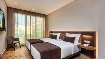 A modern hotel room with two beds, a desk, and a large window with curtains.