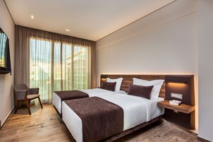 Una habitación de hotel moderna con dos camas, un escritorio y un amplio ventanal con cortinas.