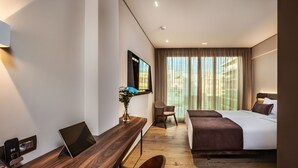 Una habitación de hotel moderna con un escritorio de madera, una cama, una silla y un televisor montado en la pared.