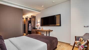 A hotel room with a large bed, a desk with a chair, a television mounted on the wall, and a wardrobe.