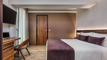A hotel room with a bed, a desk with a computer, a chair, and a TV.