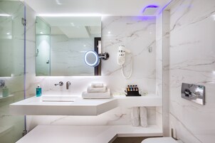 Un baño moderno con un espejo grande, teléfono integrado y tocador con lavabo y toallero.