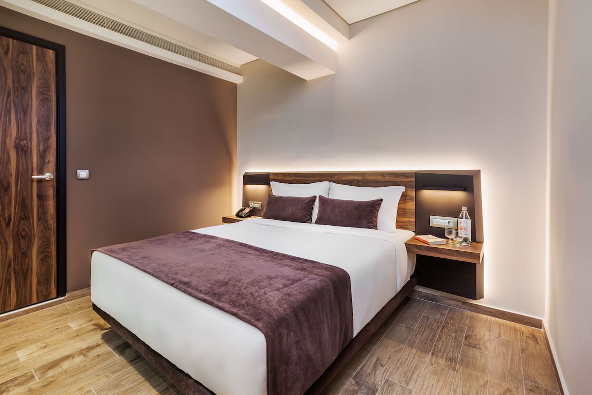 Une chambre d’hôtel avec un grand lit, une tête de lit en bois, une table de chevet avec une lampe et une petite table de nuit avec un téléphone et une bouteille.