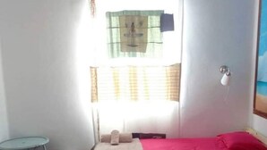 A room with two beds, a small table, and a window with curtains. - TEGUISE OLD HELMET (Teguise)