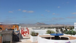 A rooftop terrace with a view of distant mountains, a mural, and potted plants. - TEGUISE OLD HELMET (Teguise)