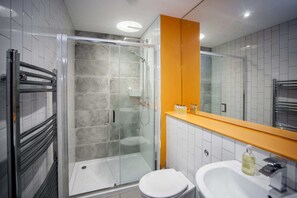 A modern bathroom with a glass-enclosed shower, a white toilet, and a sink with a mirror above it.