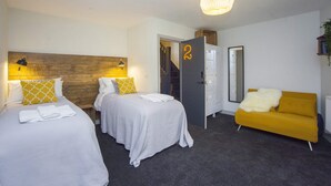 Hotellihuone, jossa on kaksi sänkyä, sohva, vaatekaappi ja portaikko.