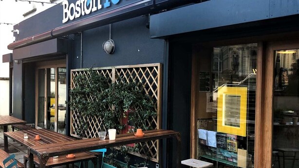 Ulkona on istuinalue, jossa on pöytiä ja tuoleja. Alue sijaitsee rakennuksen edessä, ja rakennuksen kyltissä lukee: ”Boston Tea Party”.