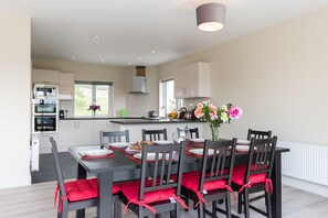 Una cocina moderna con electrodomésticos integrados, un comedor con sillas rojas acolchadas y un florero sobre la mesa.