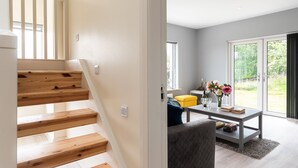 Ein modernes Interieur mit einer Holztreppe, einem Essbereich inklusive Tisch und Stühlen sowie einer Aussicht ins Freie durch große Schiebetüren.
